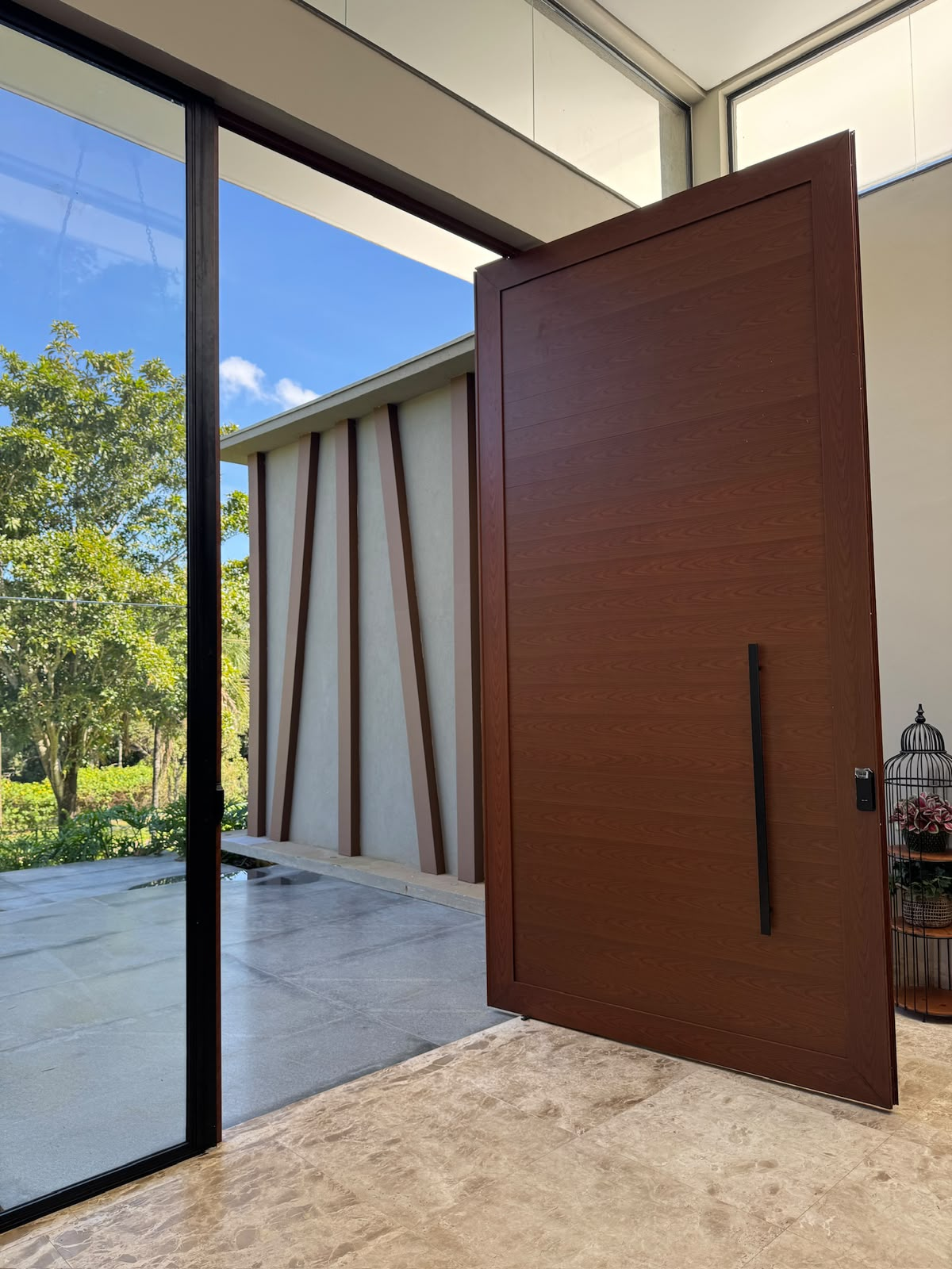 Porta pivotante aberta com vista para área externa e jardim